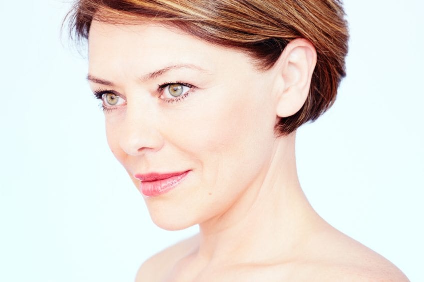 Close up portrait of beautiful middle aged woman with short brown hair, red lips and fresh makeup looking aside over blue background - beauty concept