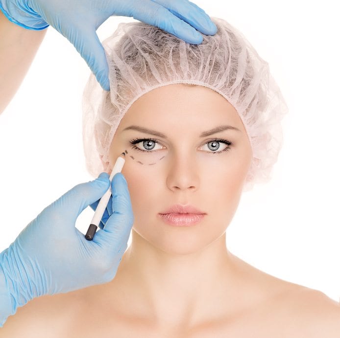 Plastic surgeon drawing lines over eyelid of a nice young female before cosmetic operation, isolated over white background.