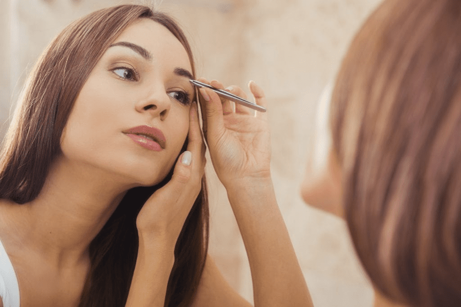 woman using tweezer on eye brow