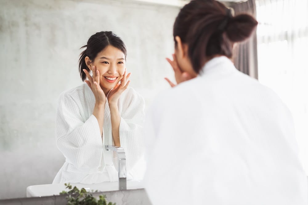 woman cleaning face front of mirror, skin care