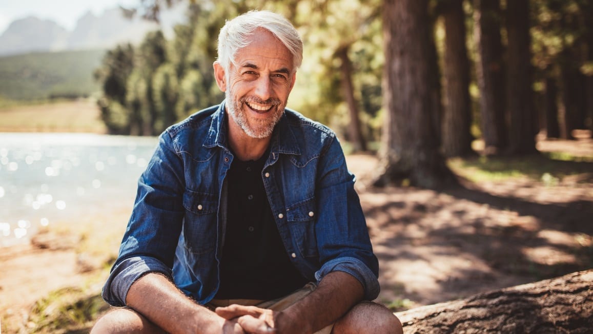 man sitting down on tree trunk smiling