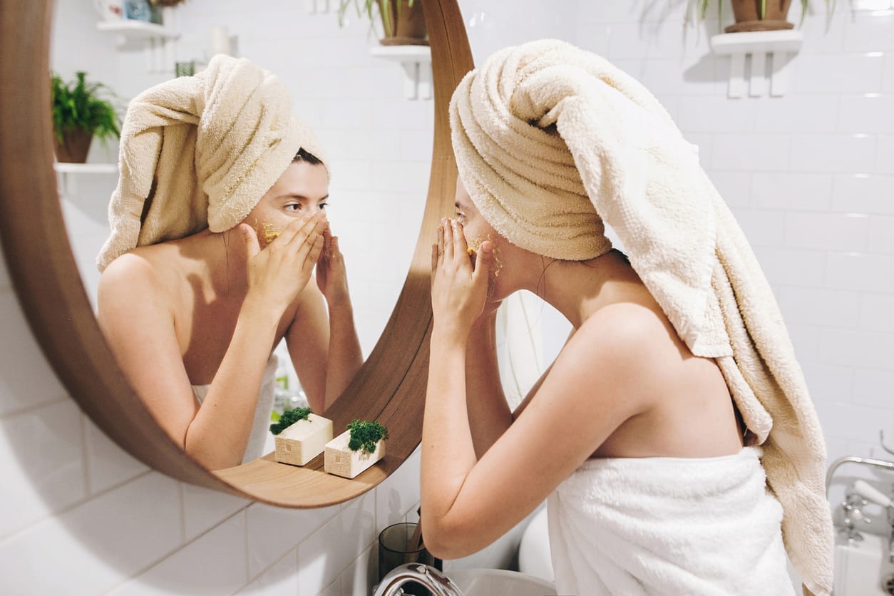 Young happy woman in towel applying organic face scrub