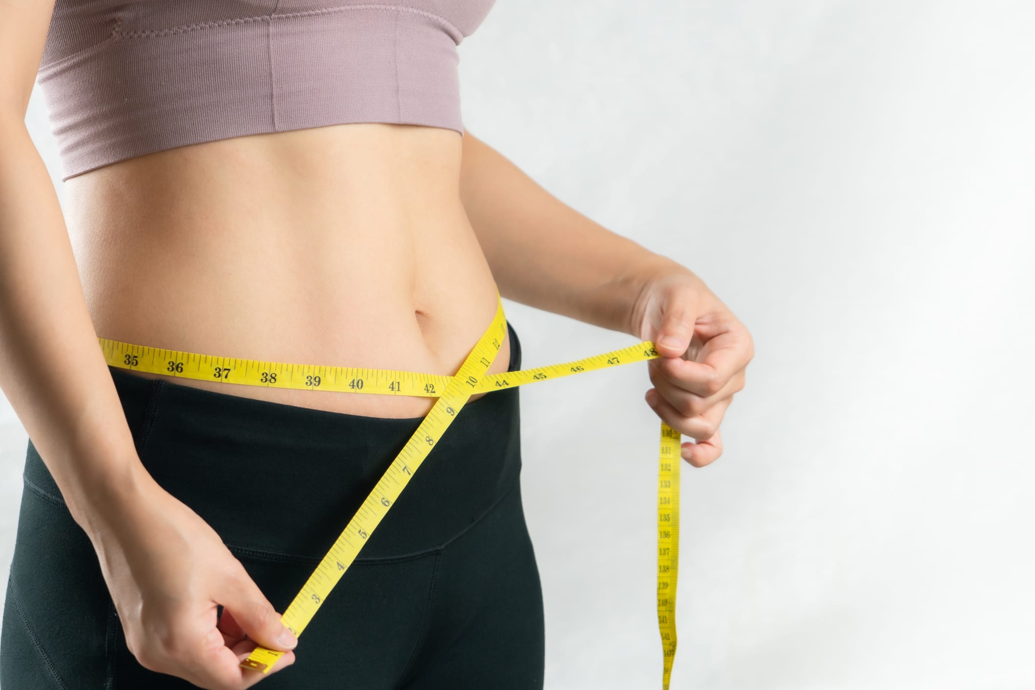 Young woman measuring her belly waist with measure tape