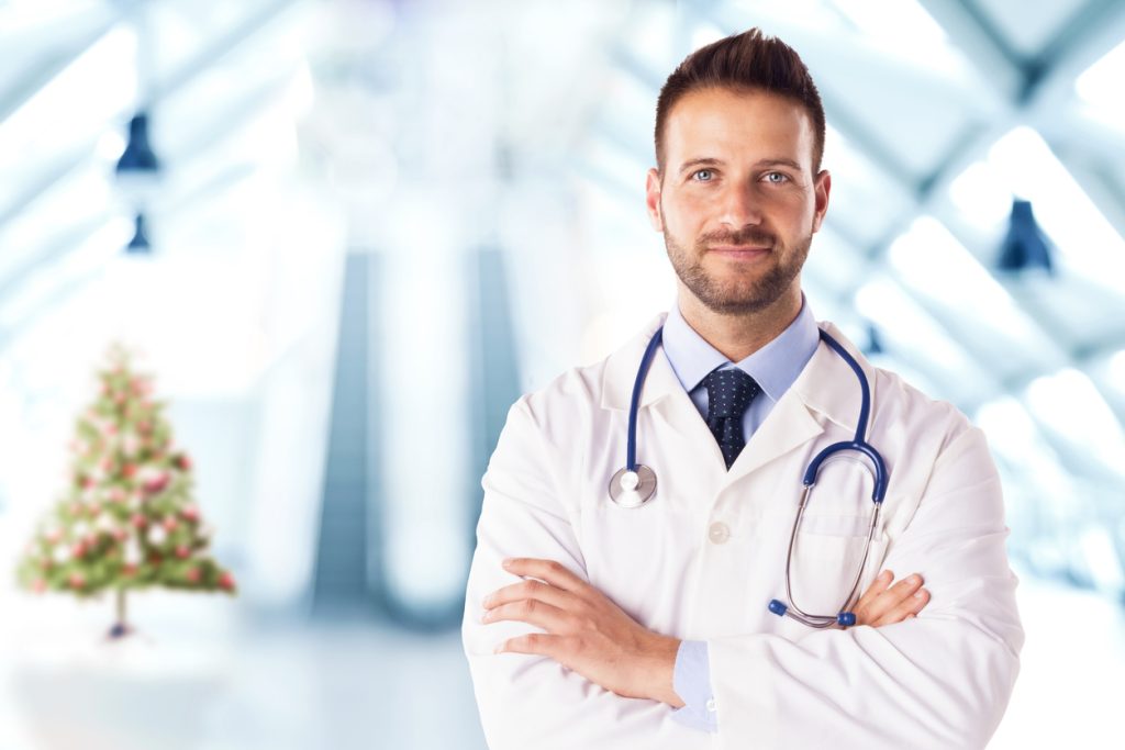 Cosmetic surgeon in a hospital stood in front of a Christmas tree