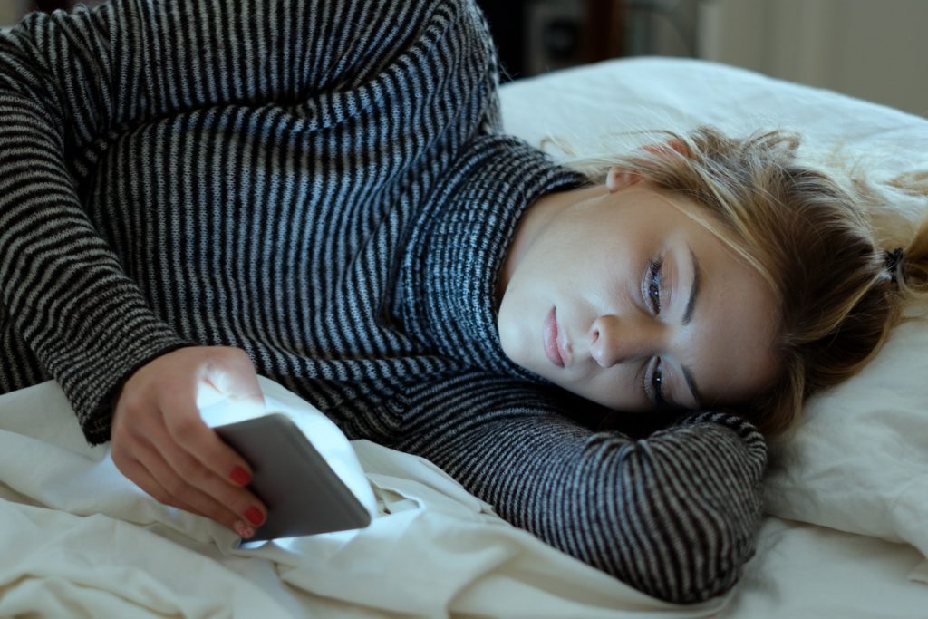 Young teenage girl scrolling on her phone in bed looking sad