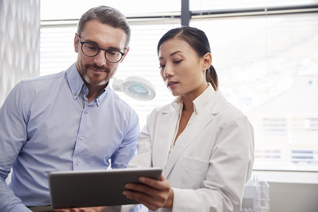 Female practitioner showing male client cosmetic surgery options on an iPad