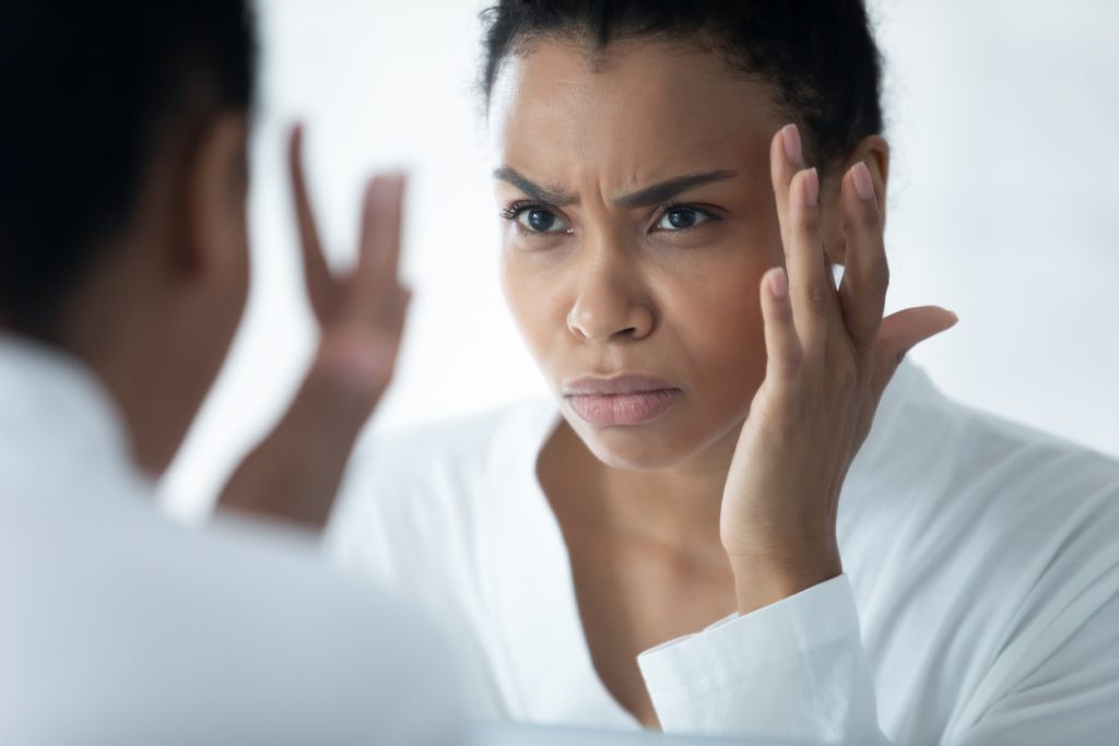 Woman looking stressed while examining skin in mirror