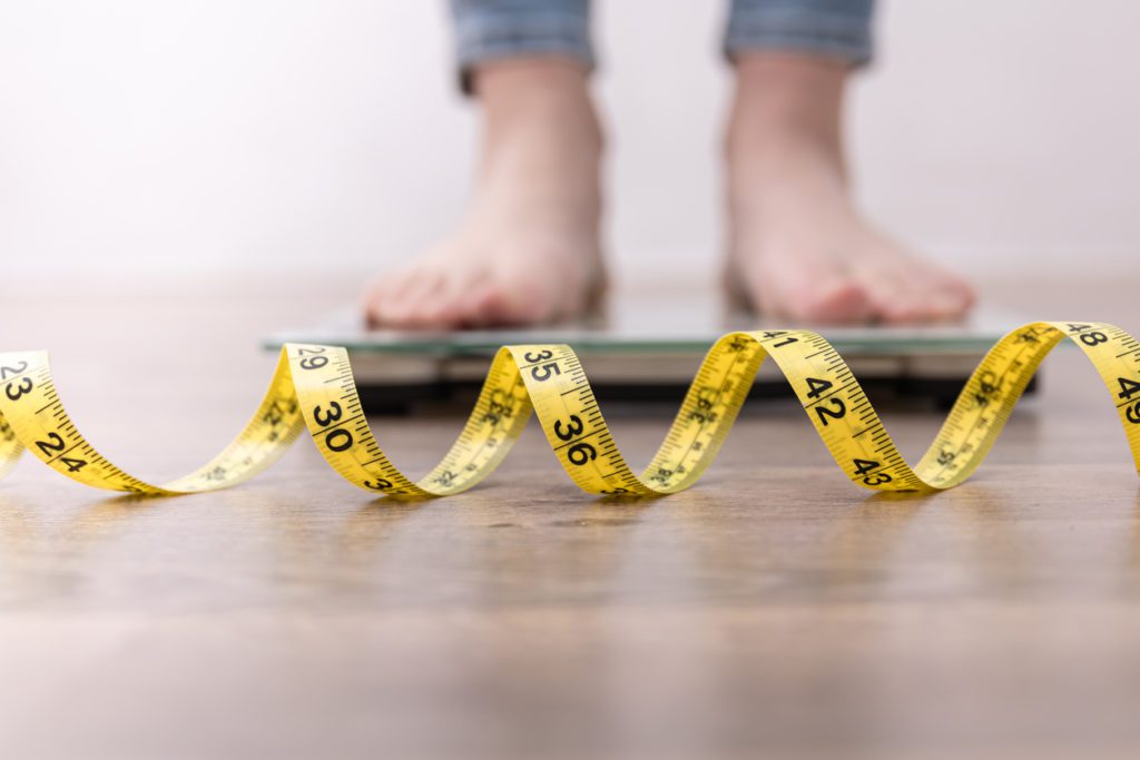 Someone stood on weighing scales with tape measure on the floor