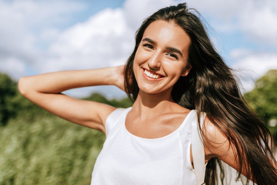Woman smiling with glowing skin in the sun outdoors in a field