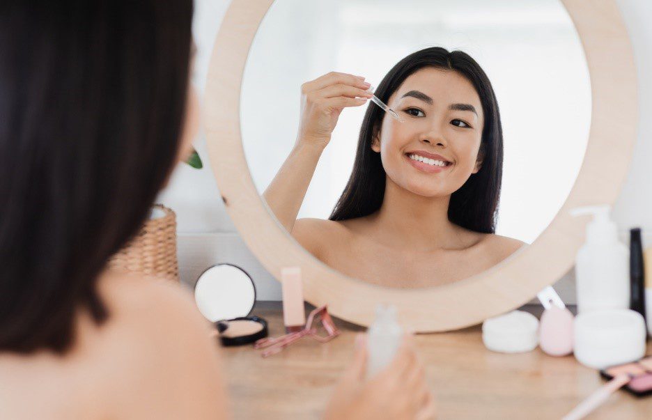 Woman smiling doing skincare routine in the mirror