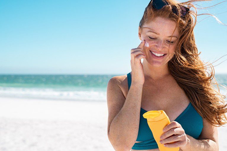 Woman at the beach smiling putting suncream on