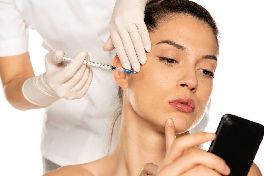 woman getting dermal fillers while scrolling on a phone